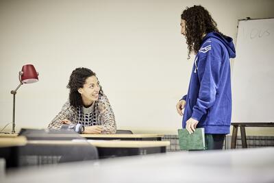 Deux comédiens, une jeune femme et un jeune homme, discutent dans une salle de classe