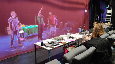 Sur scène, des comédiens vérifient les branchements des lumières.