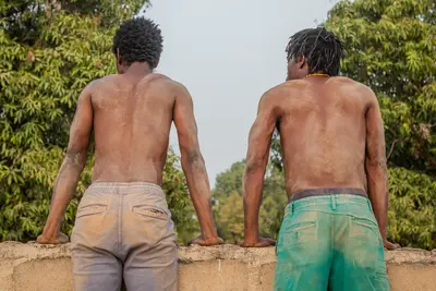 Deux hommes torse-nu sur un mur, de dos.
