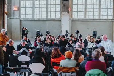 Une femme joue de la musique électronique avec des enceintes, entourée de spectateur·trices assis·es autour d'elle.