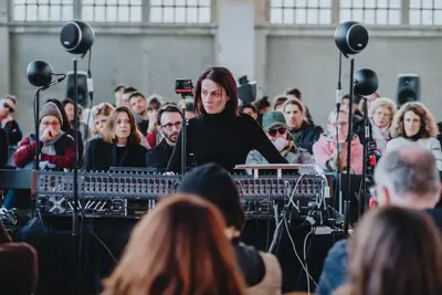Une femme joue de la musique électronique avec des enceintes, entourée de spectateur·trices assis·es autour d'elle.