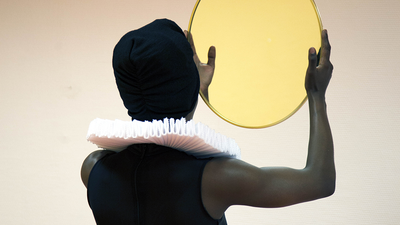 Une femme noire de dos, regarde un miroir.