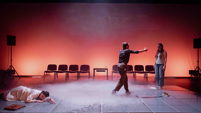 Trois comédiennes sur scène. Deux semblent se disputer tandis qu'une autre git sur le sol.