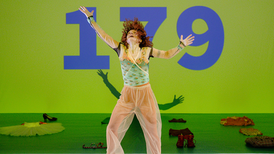 Une danseuse dansant devant un écran vert avec le nombre "179" inscrit dessus.