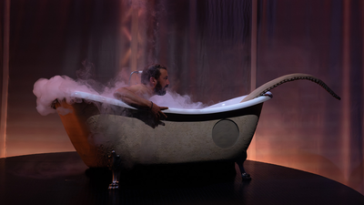 Un homme dans une baignoire sur scène, avec un tentacule.