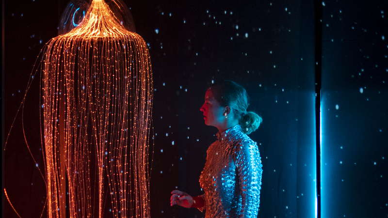 Une femme en tenue de plongée, à côté d'une méduse lumineuse.